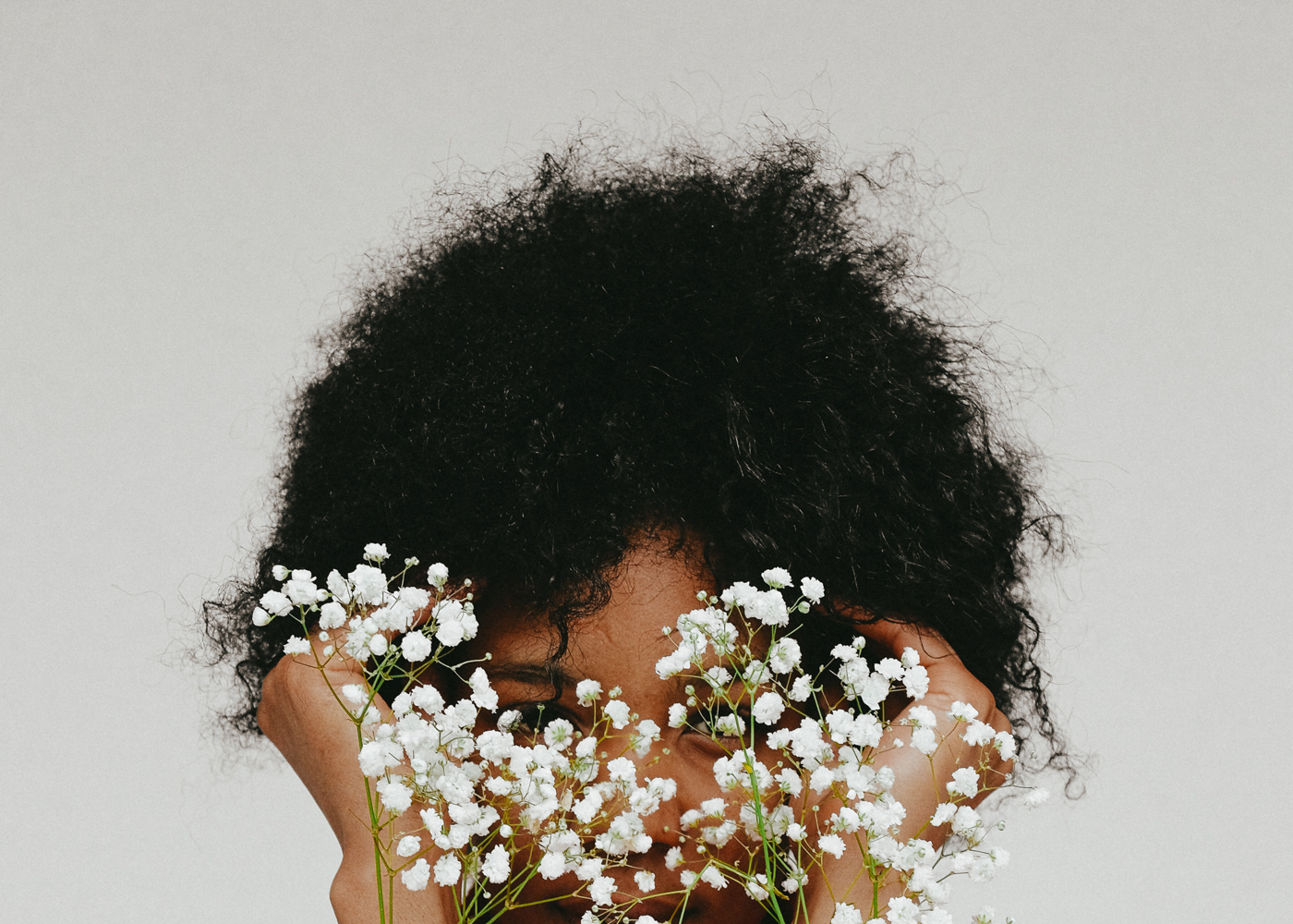 Frau mit Afrohaare deckt ihre Gesicht mit weiße Blumen